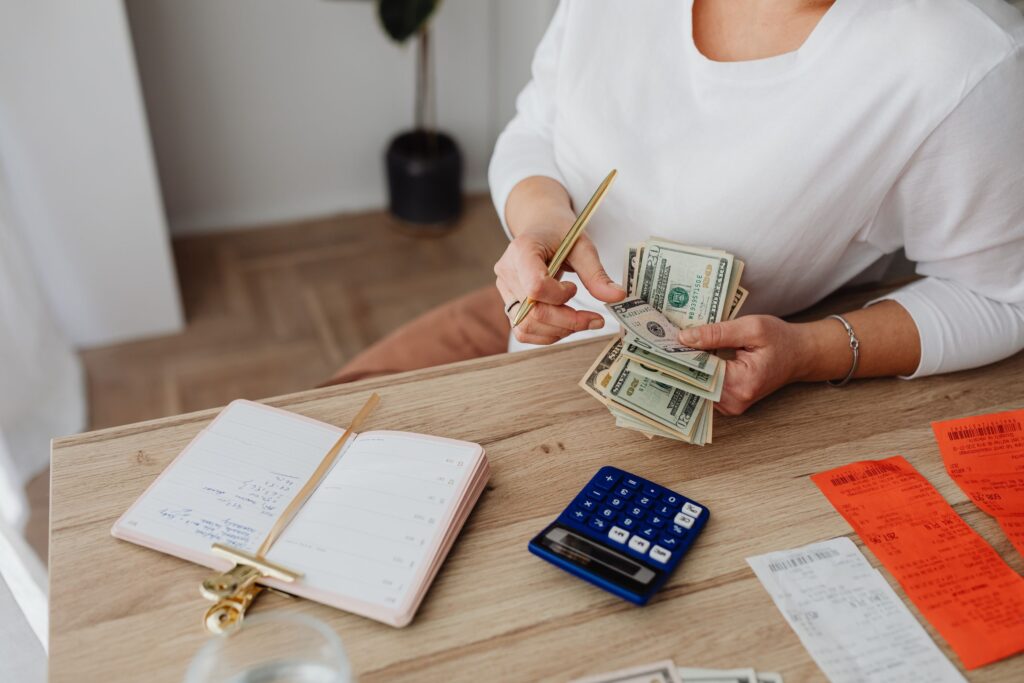 Retiree counting cash at a kitchen table beside bills, a notebook and a calculator