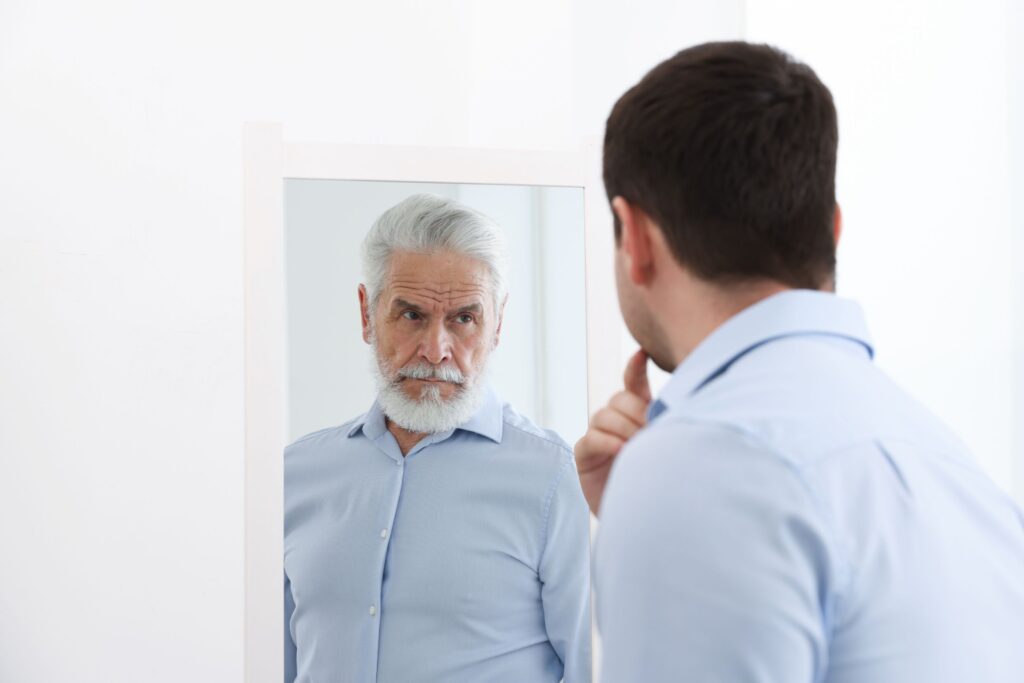 A man looking into a mirror and seeing his older self, a metaphor for taking honest stock